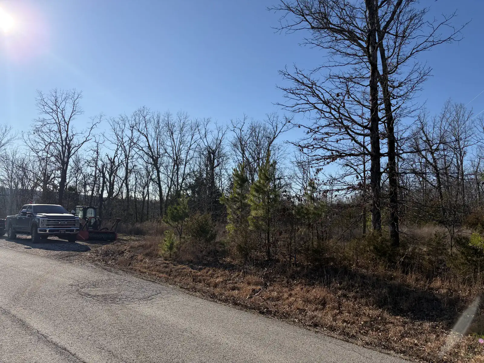 Compact track loader and a pickup parked at the edge of the standing timber on a roadside job in Northeast Arkansas