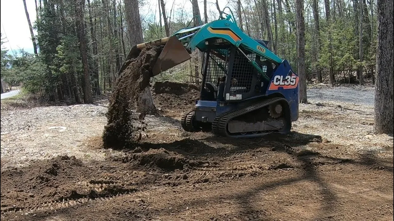 Compact track loader dumping a bucket of fill dirt onto a rough spot in a cleared yard