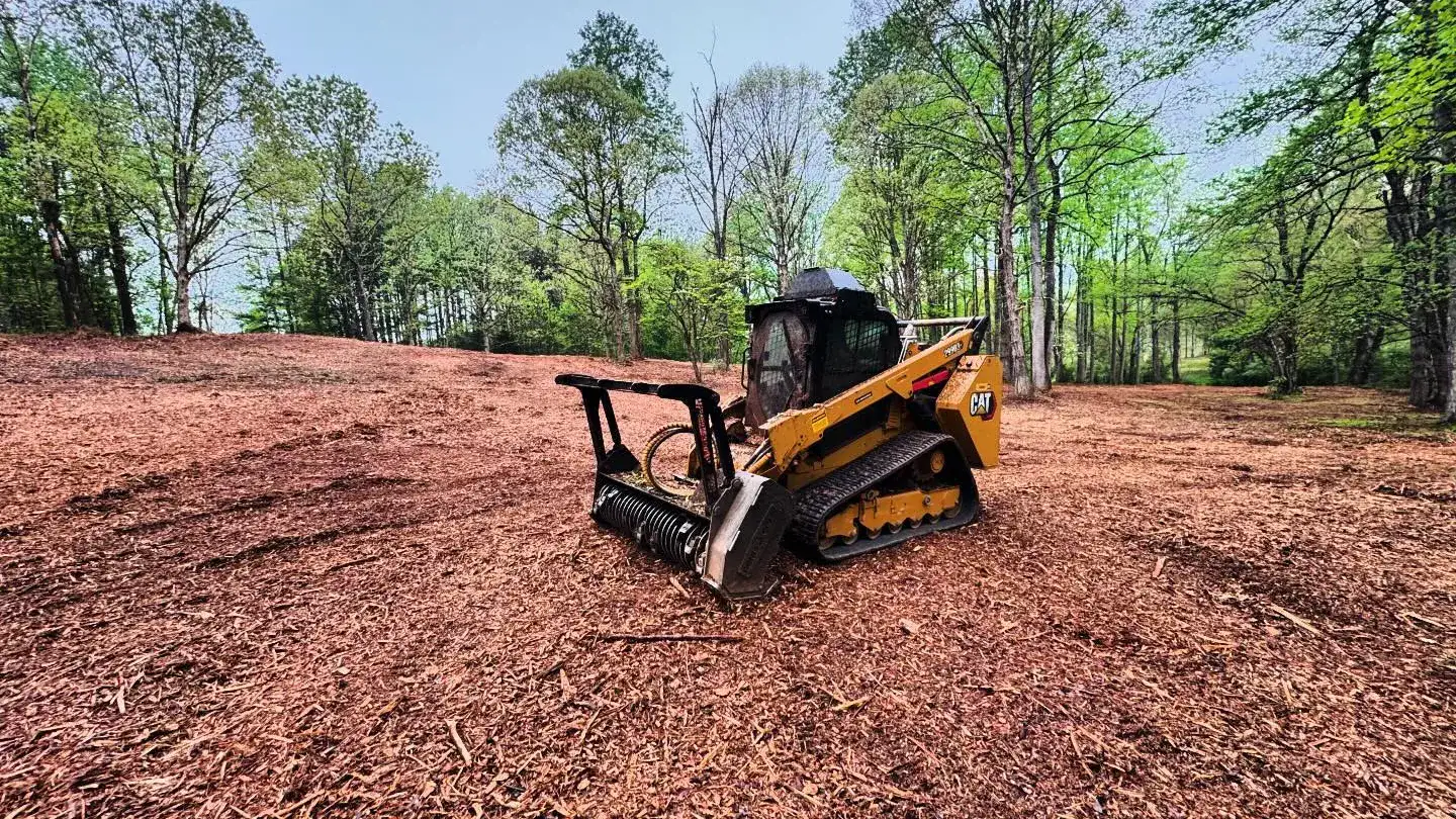 Compact track loader with a mulcher head sitting on a wide lot carpeted in fresh mulch