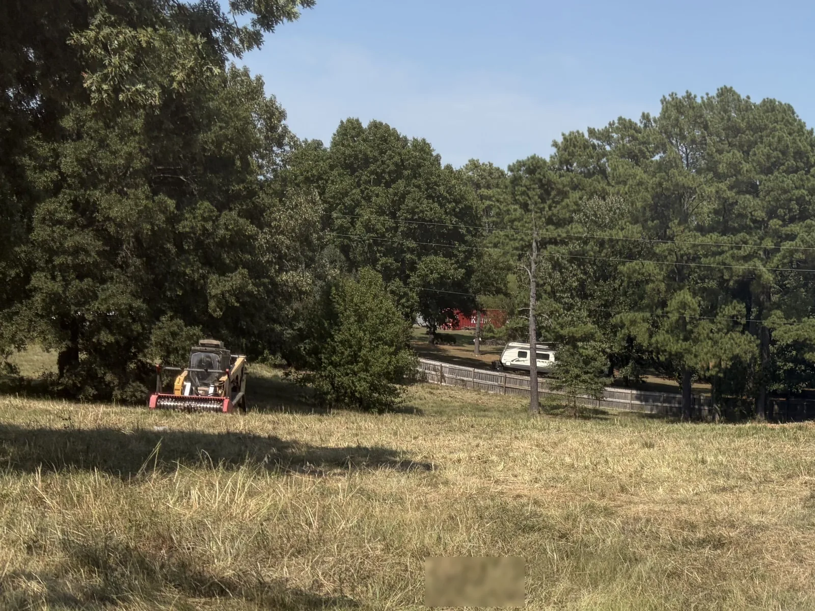 Cleared grassy lot with the treeline pushed back and a track loader working at the far edge in Northeast Arkansas